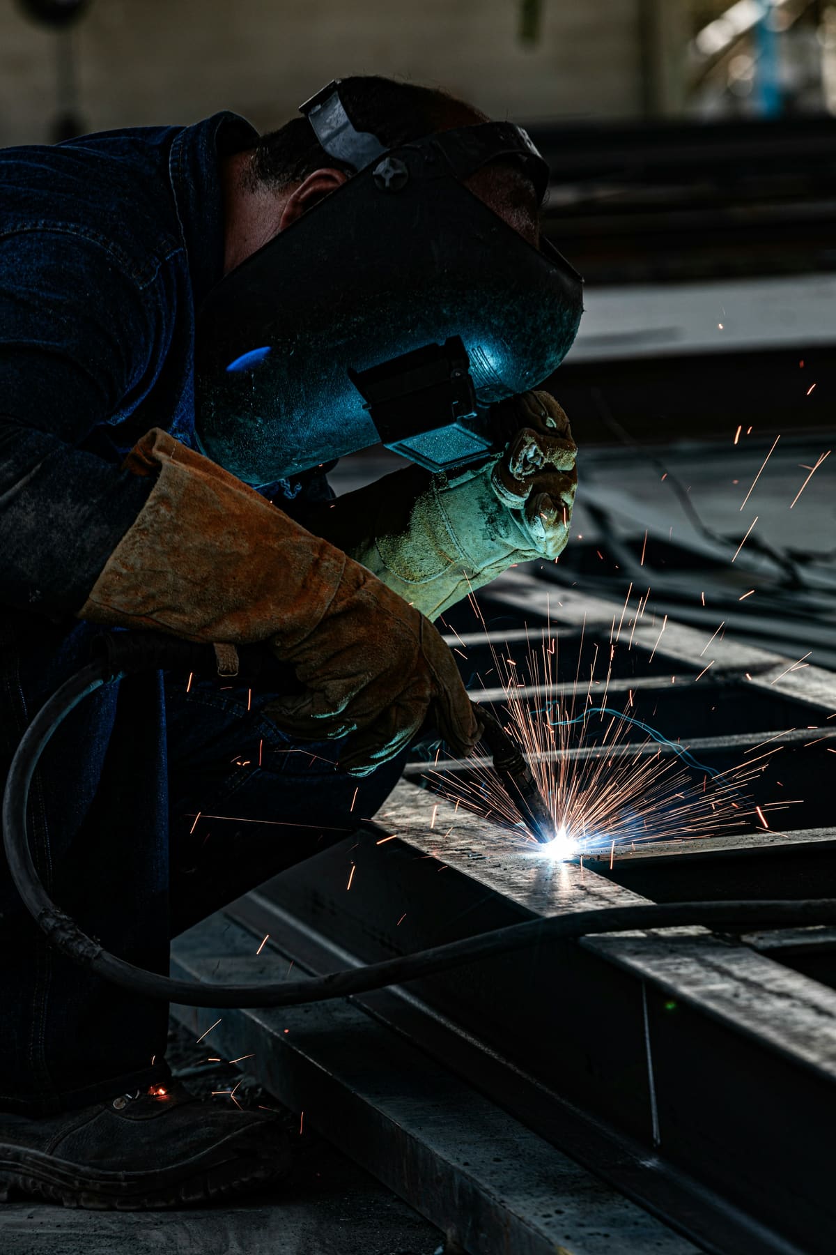 Welder in a protective hood striking an arc on steel bar stock, sparks flying